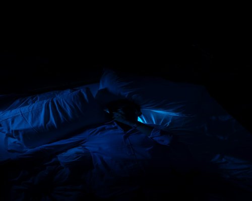 Person using smartphone in bed with blue light effect