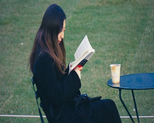 A person holding a warm cup of tea and reading a book